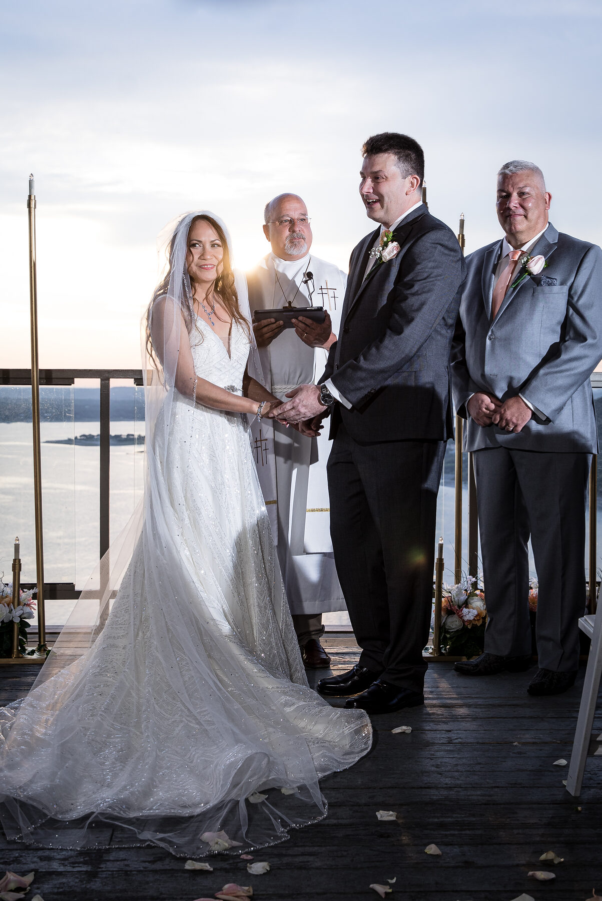 A sunset ceremony on the rooftop deck at The Oasis at Lake Travis — couple holding hands as the sun dips behind the lake
