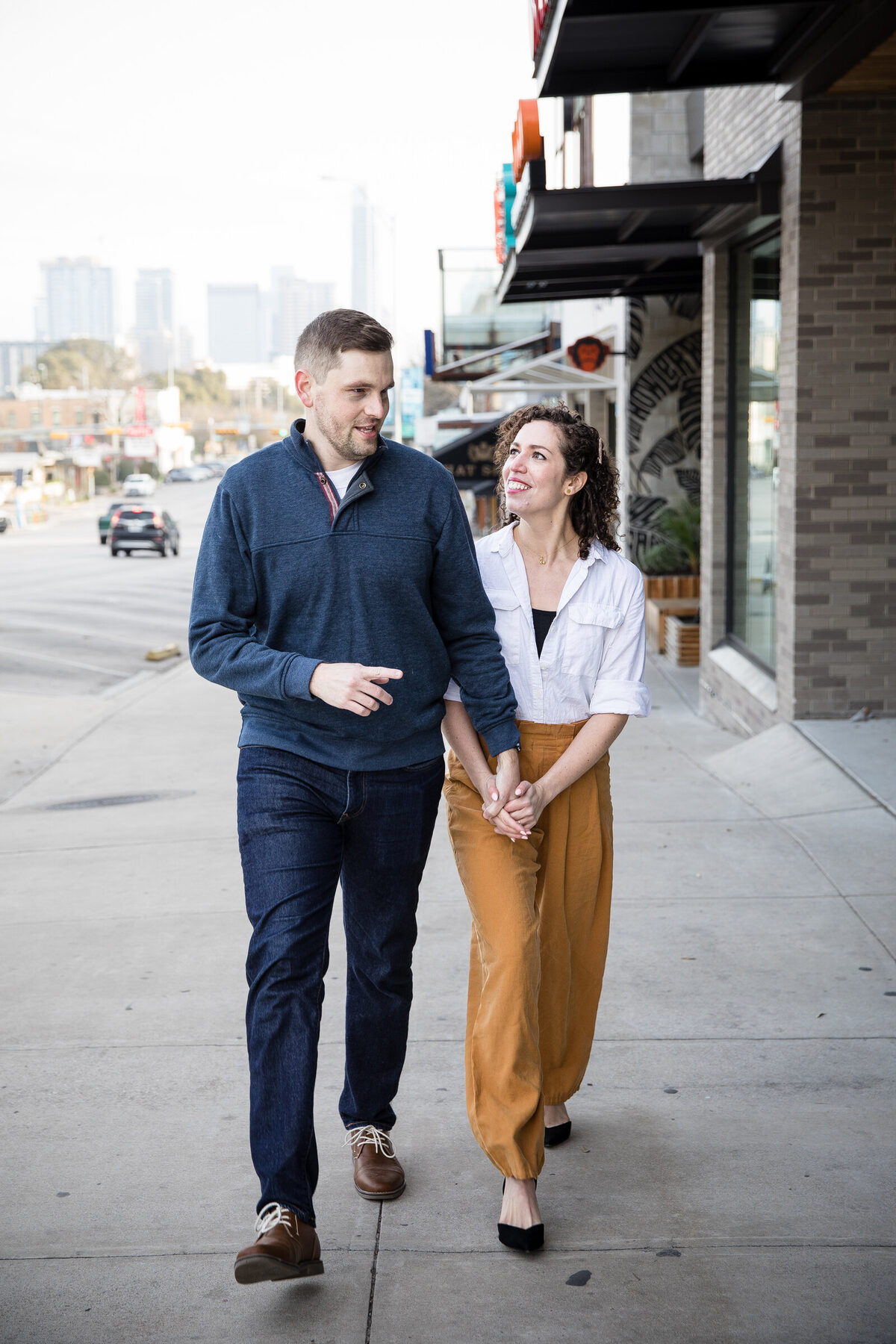Couple walking hand-in-hand down an Austin street with the downtown skyline behind them — proposal photography in Austin, TX
