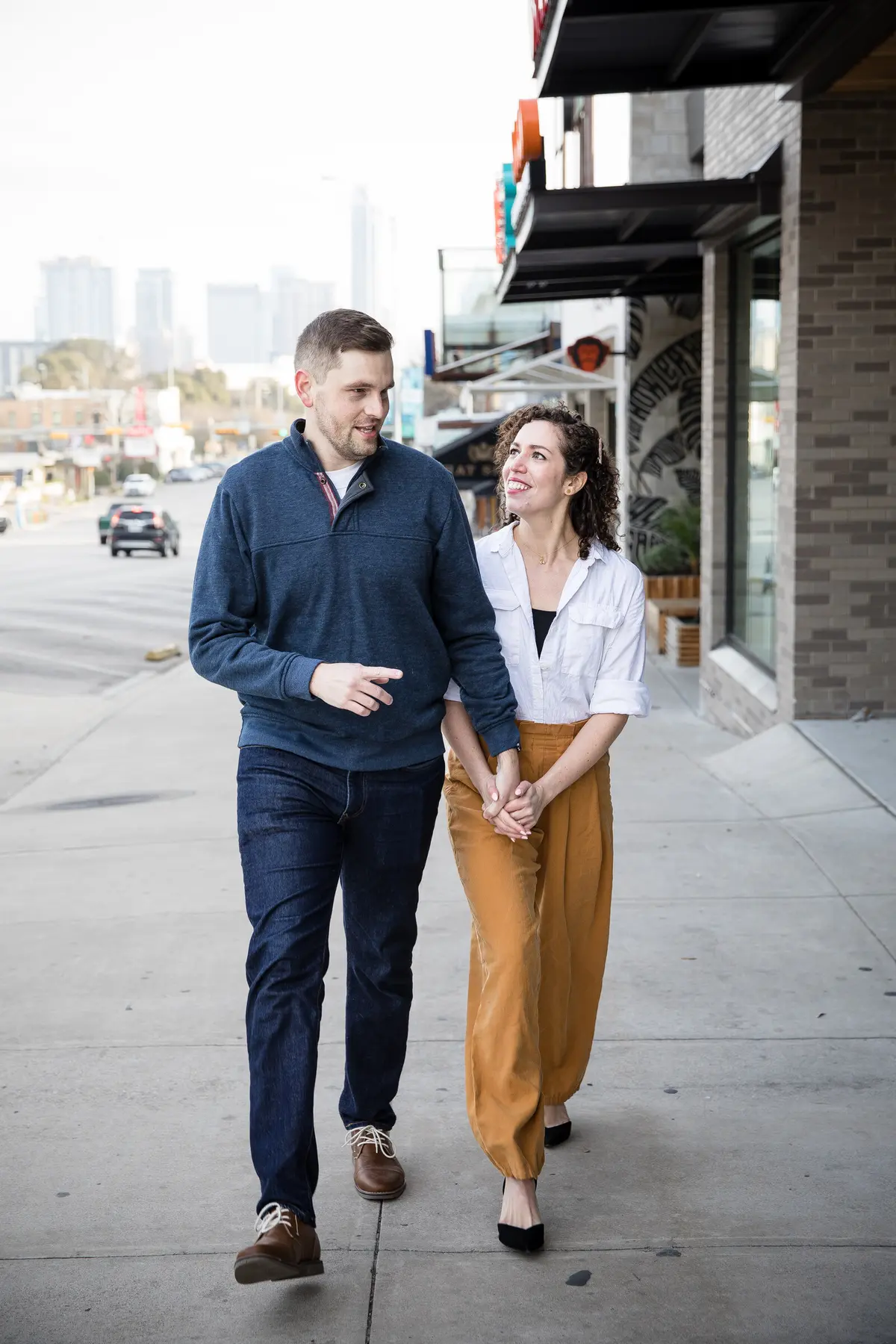 Couple walking hand-in-hand down an Austin street with the downtown skyline behind them — proposal photography in Austin, TX