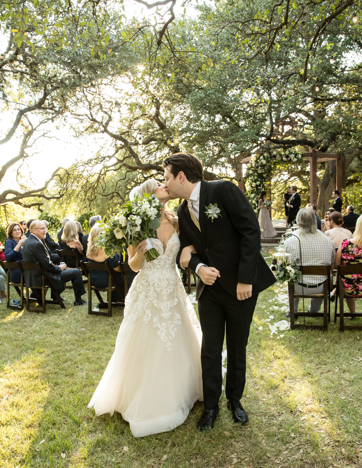 A couple sharing a recessional kiss in soft golden-hour light under live oak trees — a wedding photographer's ability to work in this light is what separates pros