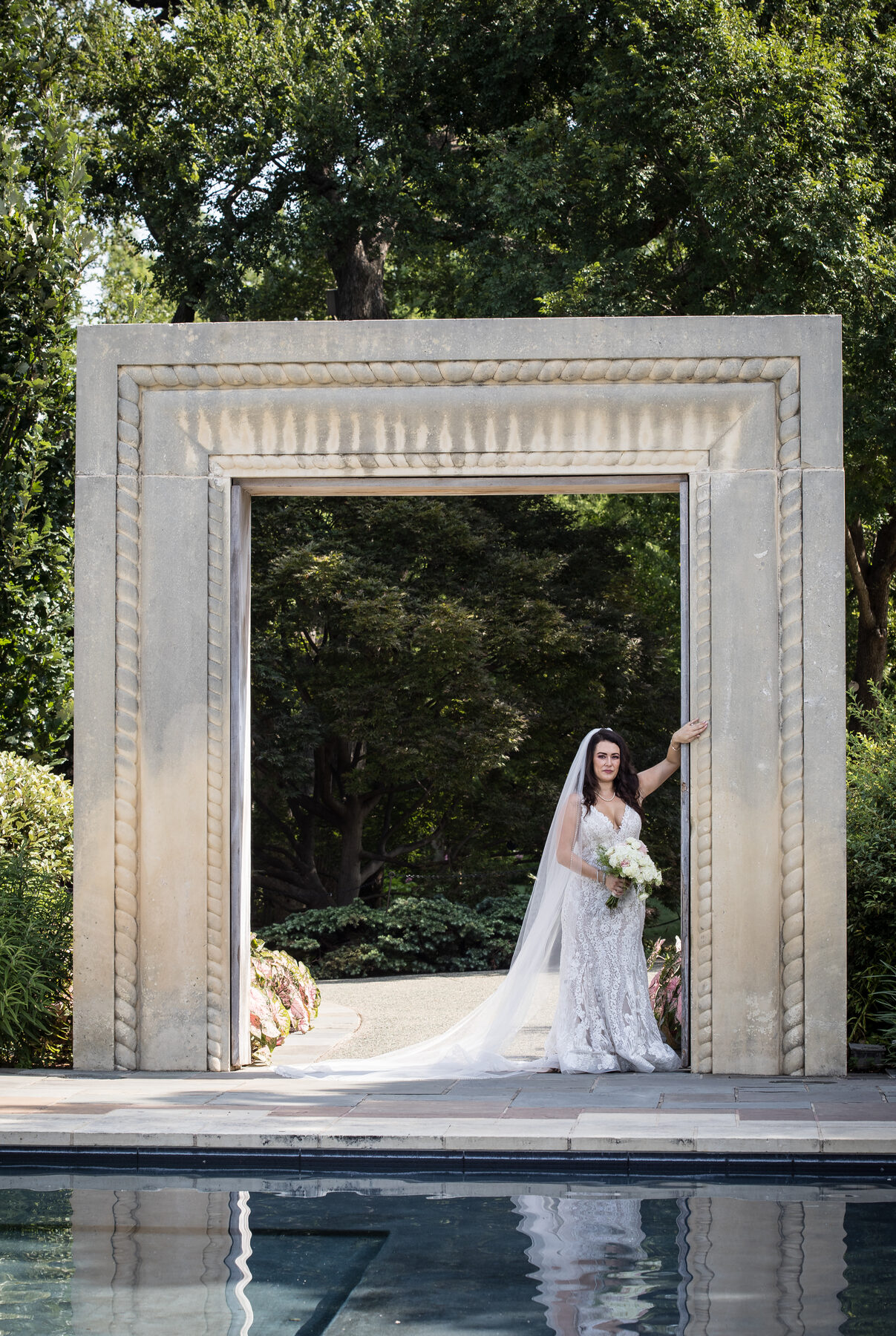 Bride at large stone garden archway over a pool