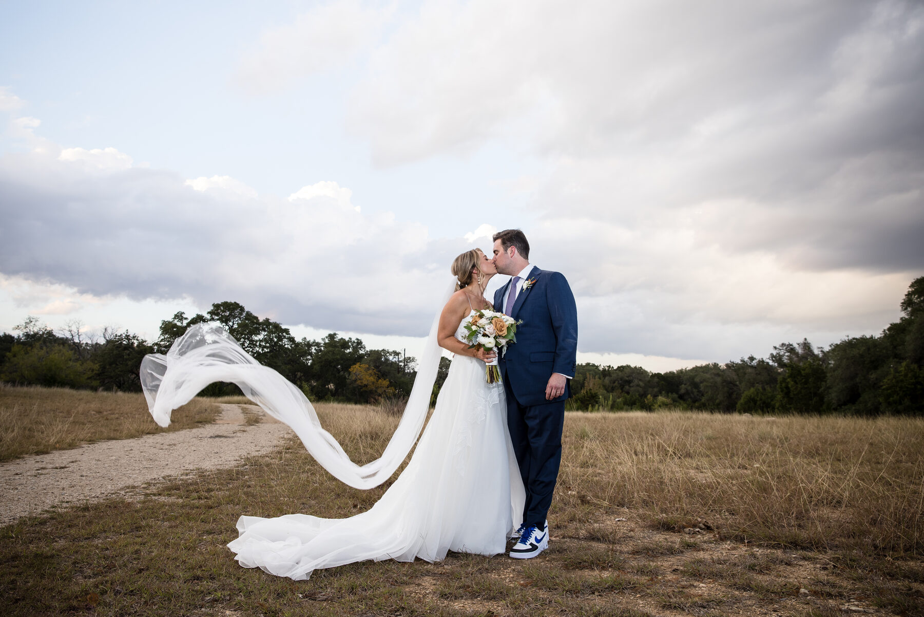 Couple kiss with veil flying in a Texas field