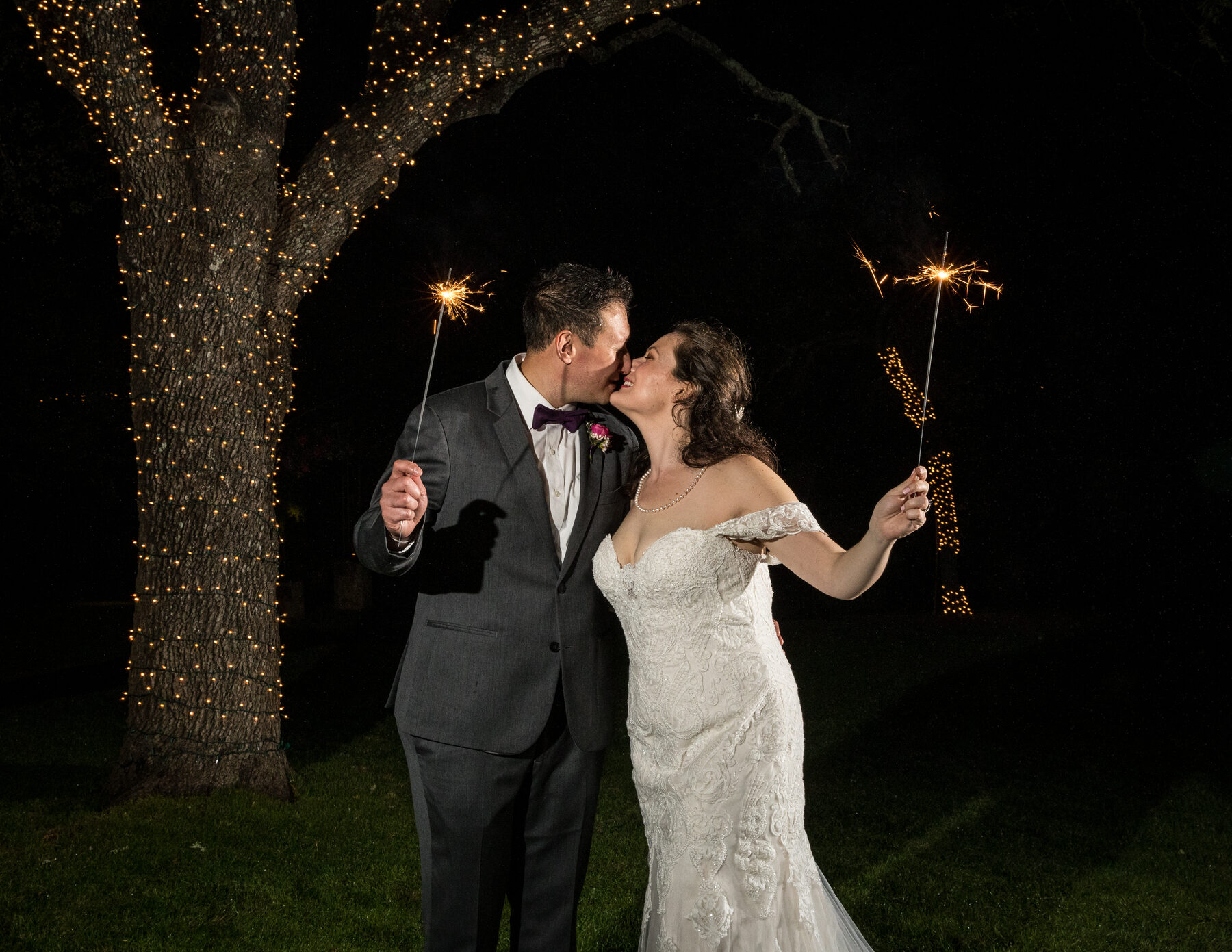 Couple kissing with sparklers under string-lit oak