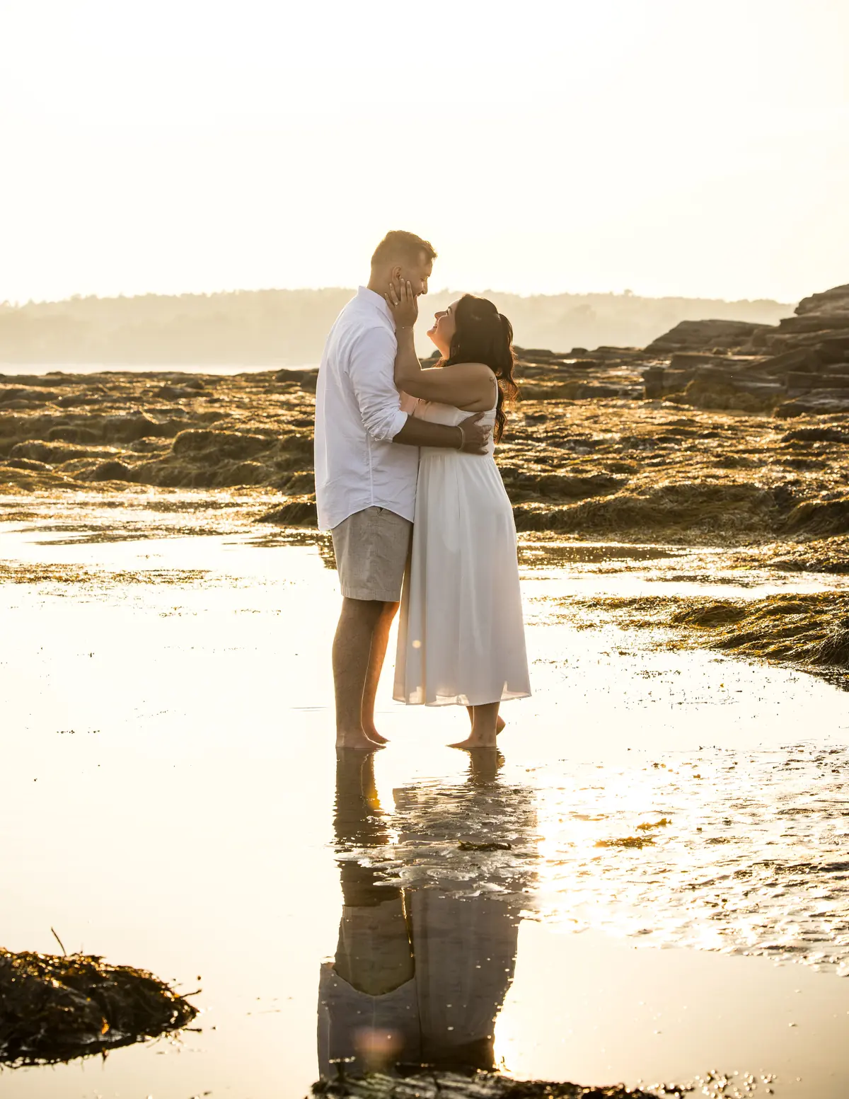 Engaged couple embracing barefoot in a tidal pool at golden hour, Kettle Cove, Cape Elizabeth, Maine
