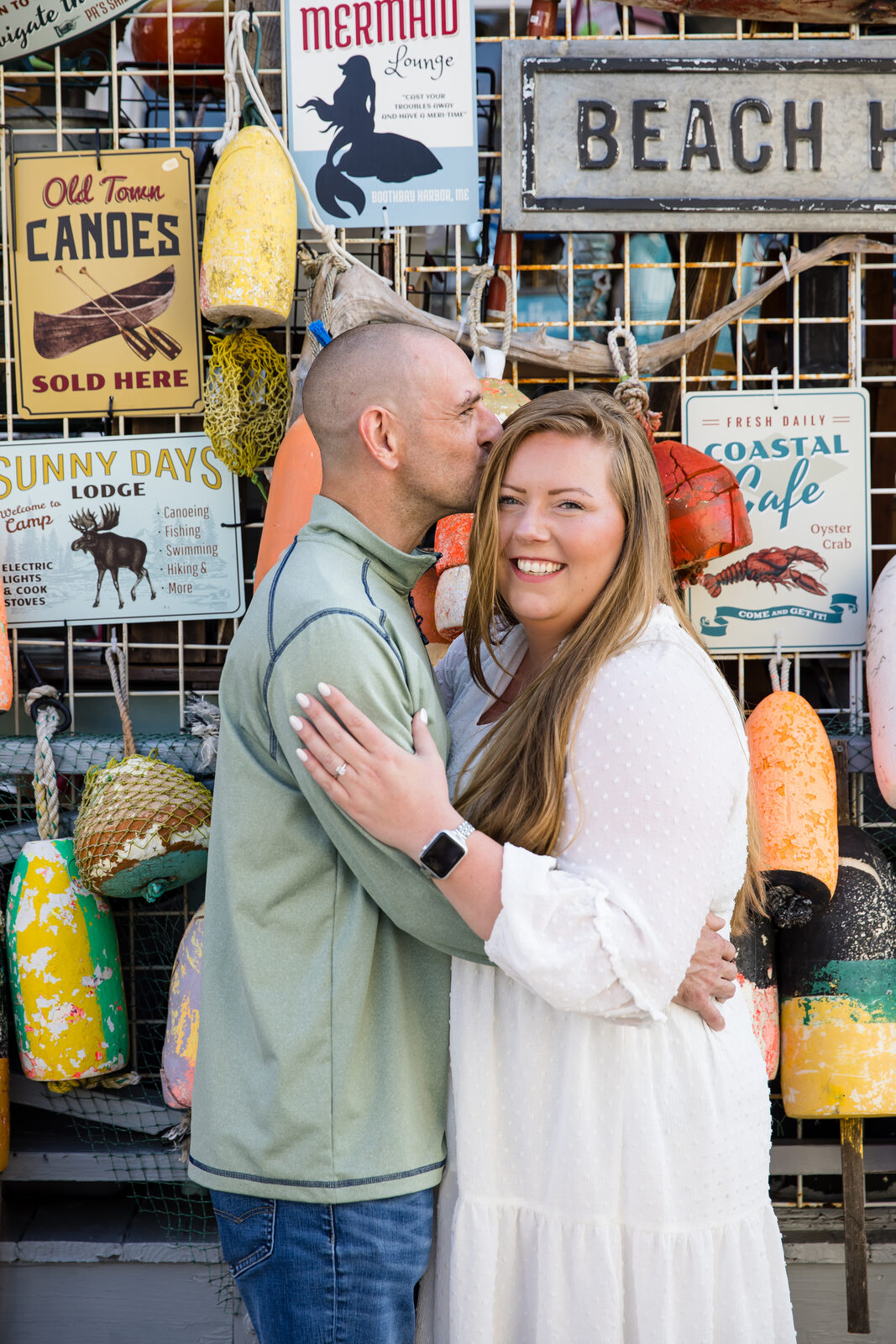 Couple embracing by a colorful lobster-buoy wall on the coast