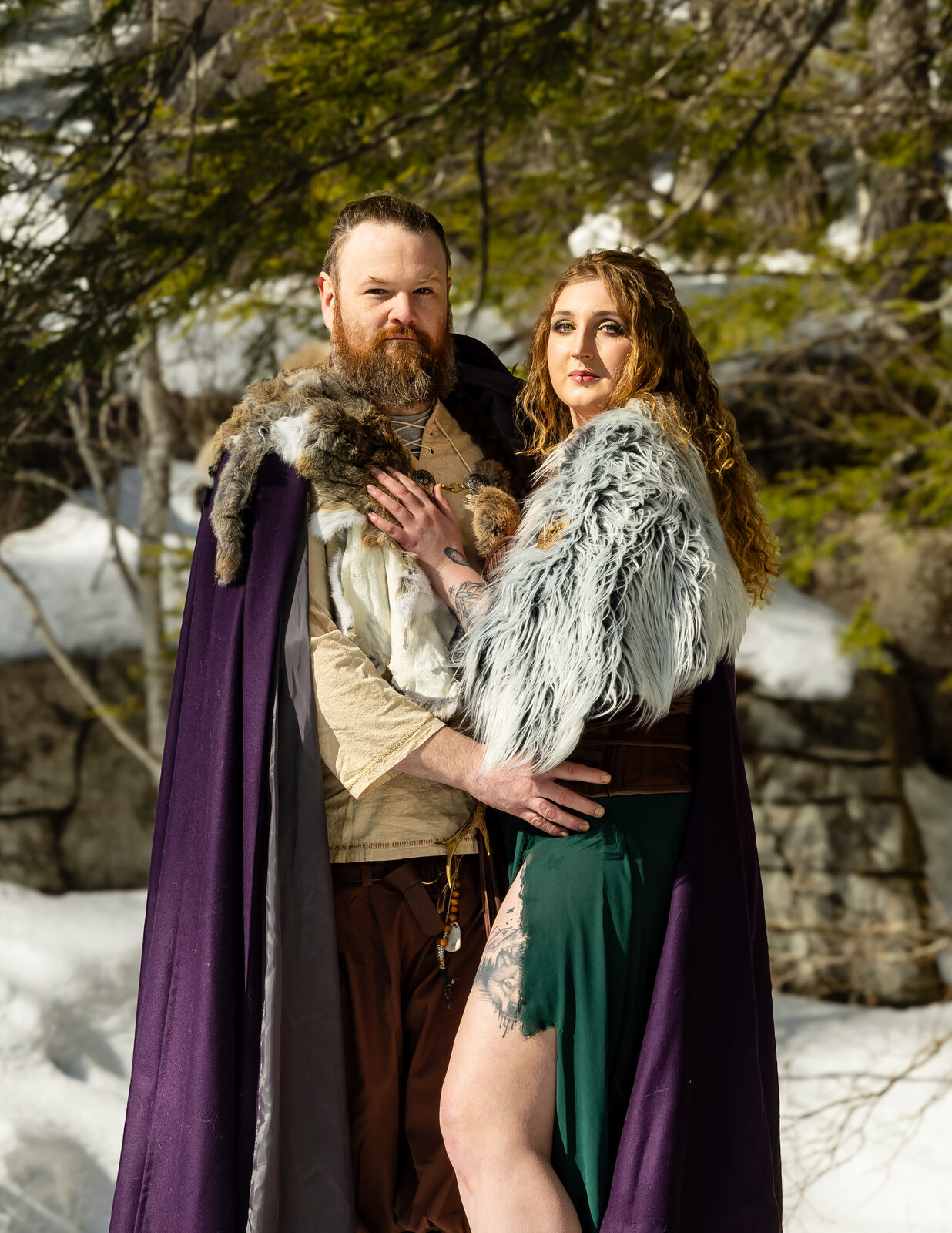 Couple in fur-trimmed Viking cloaks in a snowy forest