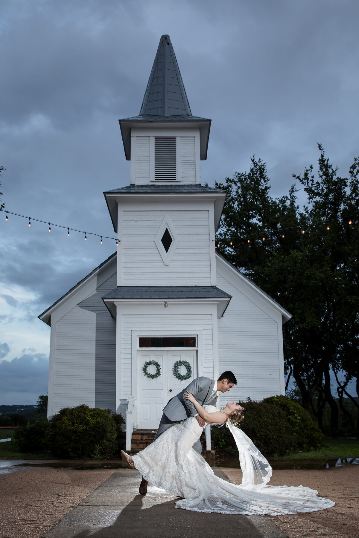 Couple dip kiss outside white chapel at dusk