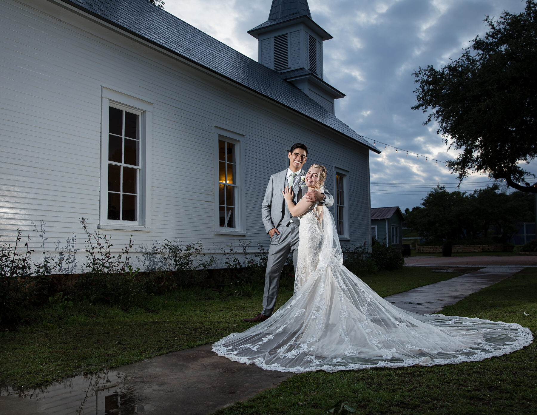 Bride with long train and groom outside white chapel