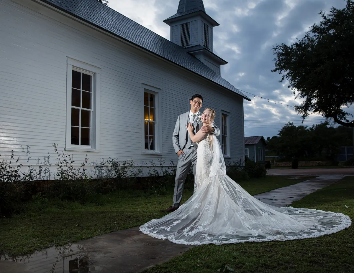 Bride with long train and groom outside white chapel