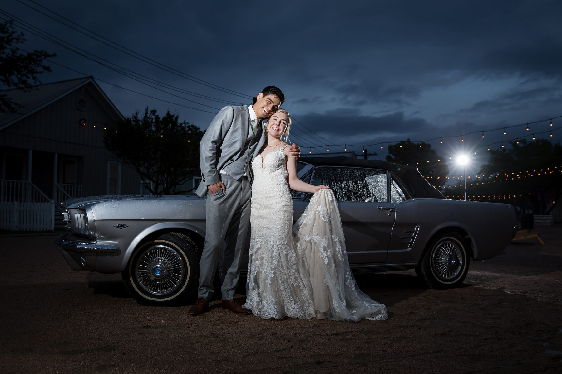 Couple by vintage Mustang at dusk, string lights