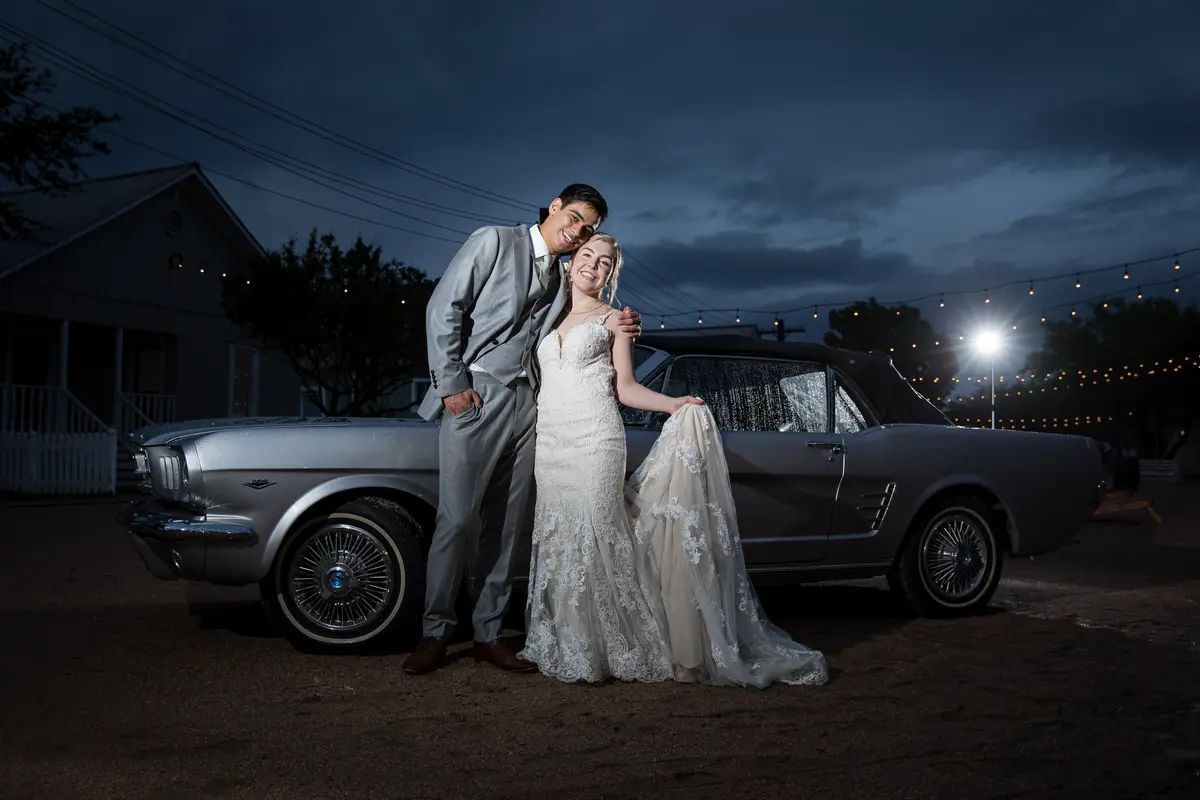 Couple by vintage Mustang at dusk, string lights