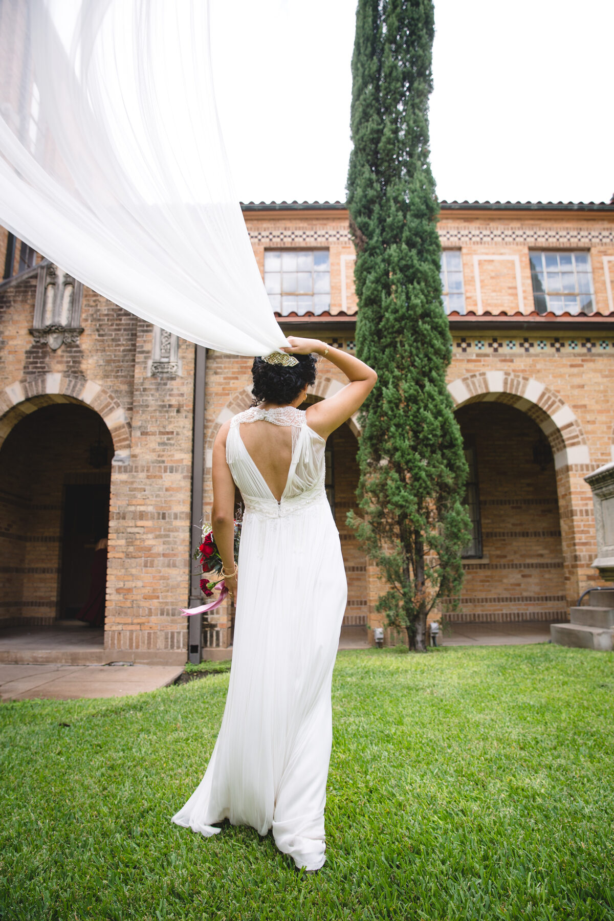 Bride from behind veil flowing at brick courtyard
